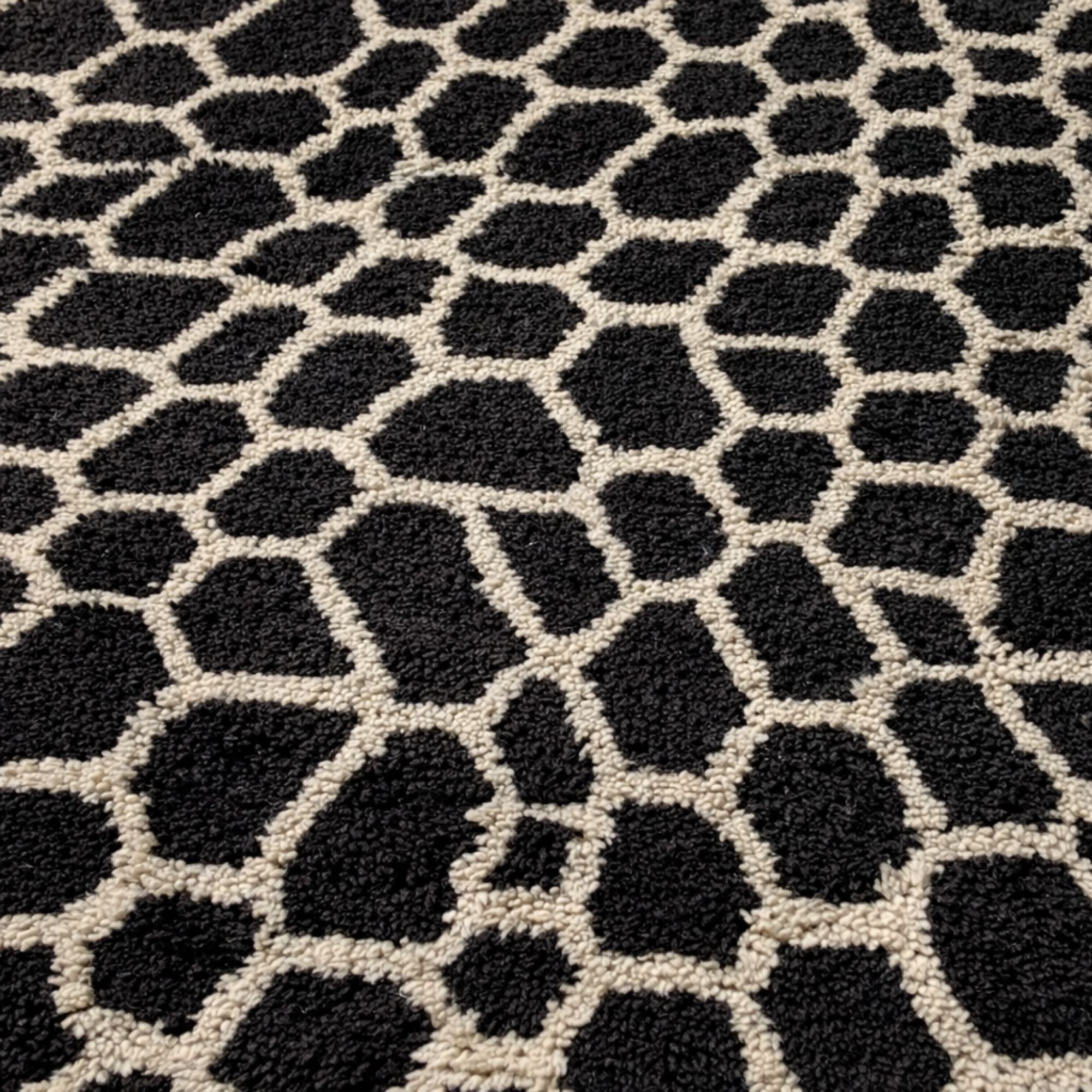 Extreme close-up of a hand-knotted Moroccan wool rug featuring plush black pile and ivory wool channels. The image emphasizes softness, depth, and natural wool texture.