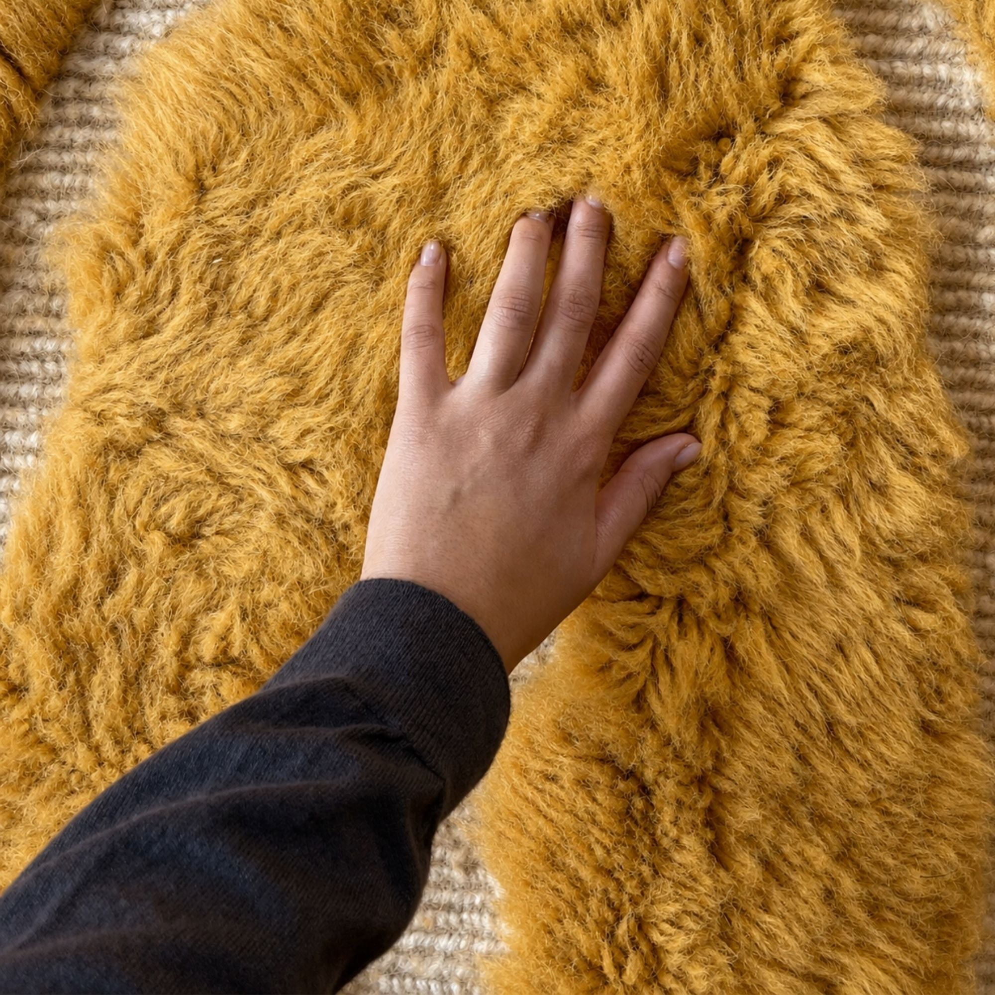 Hand touching the deep wool pile of Sahara Symphony No. 02, showcasing its exceptional softness and luxurious natural texture.