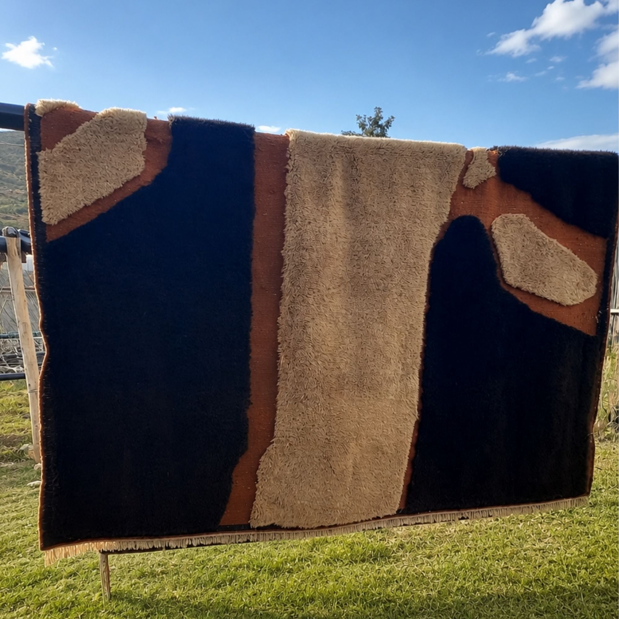 Handwoven Moroccan wool rug, Totem no. 01 design shown fully outdoors, sculptural cream and black shapes on rust ground.