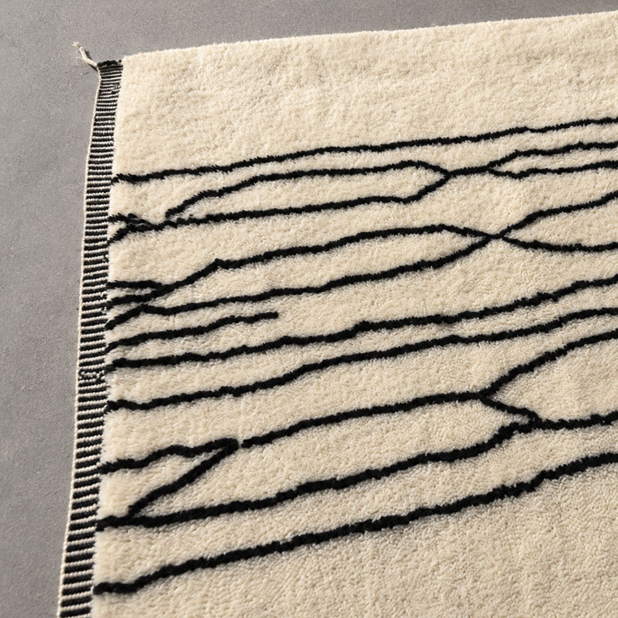 Detail of Reed Line handmade Moroccan wool rug corner showing striped flatwoven border and fringe.