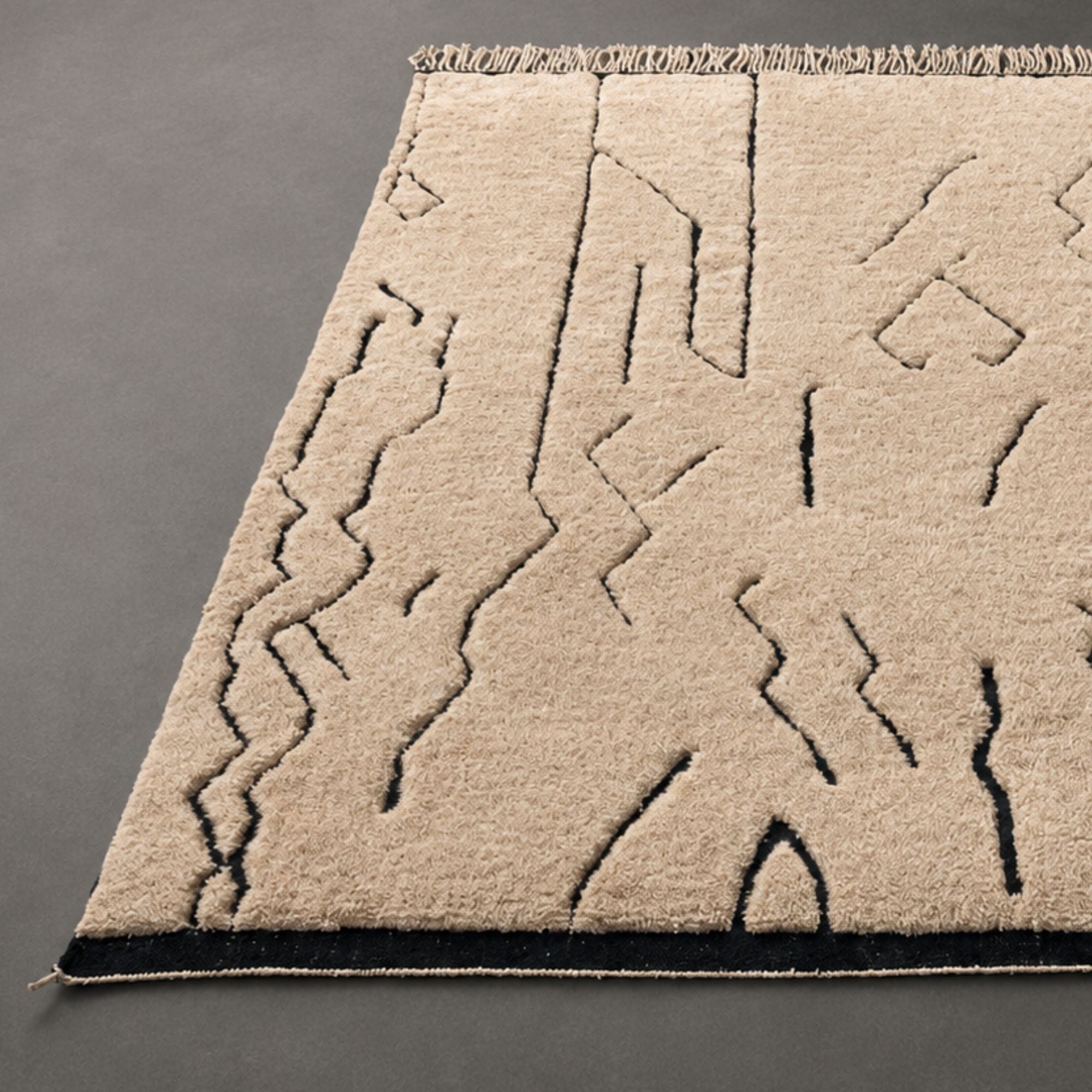 Detail of Tracks handmade Moroccan wool rug corner showing black border and fringe.