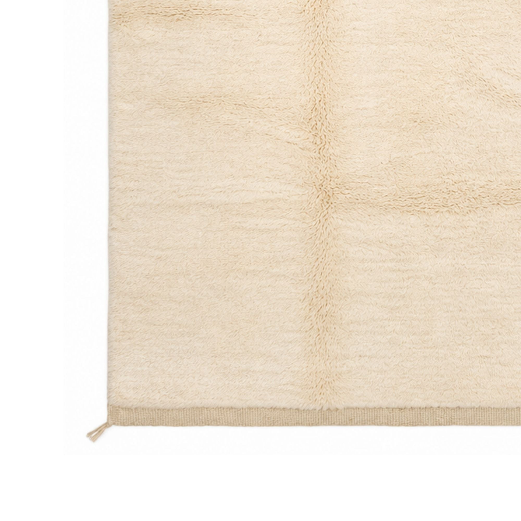 Detail of Épure handmade rug edge with soft cream wool pile and clean woven border finish