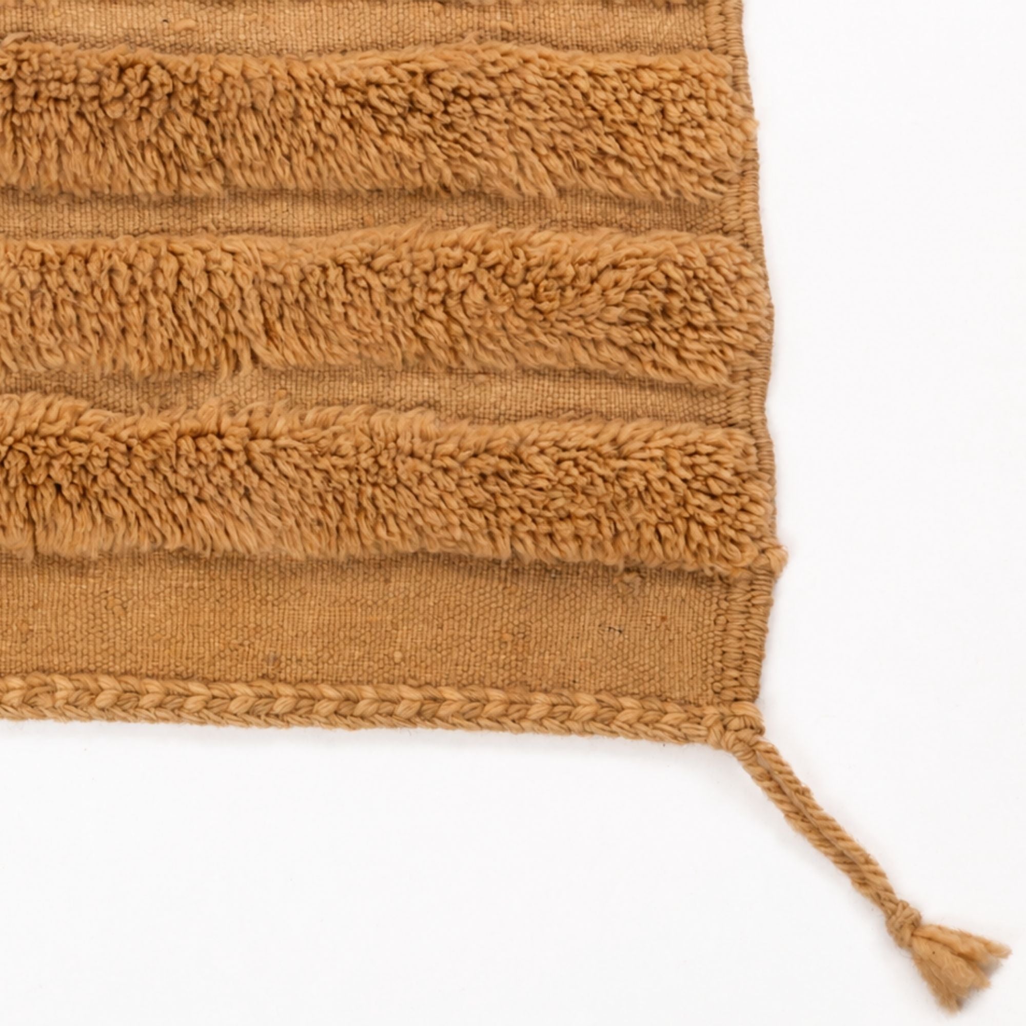 Detail of handmade Moroccan rug edge with braided finish and tassel, Strata No. 02 in warm camel wool