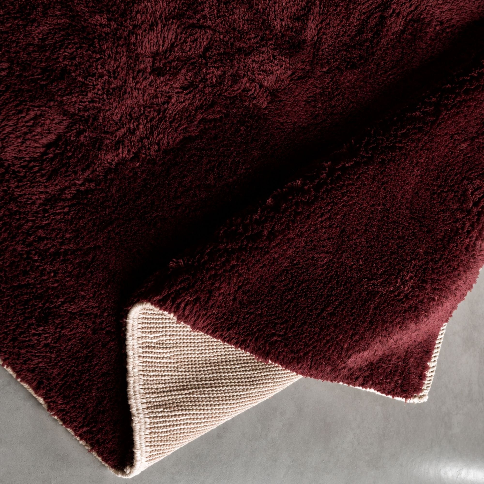 Folded burgundy Moroccan rug revealing thick handwoven wool pile, artisanal backing, and luxurious texture in deep wine red and ivory tones.