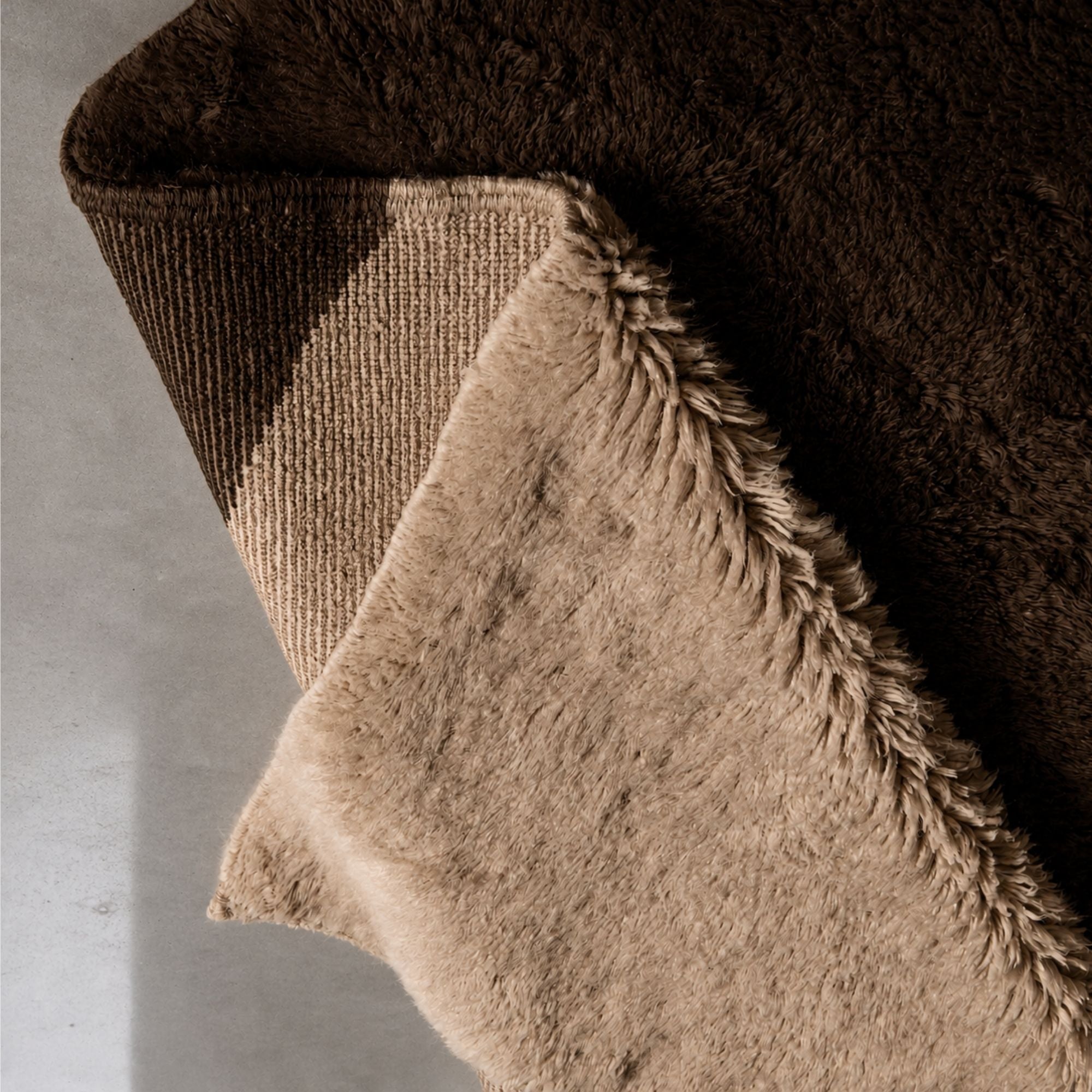 Folded handmade Moroccan wool rug revealing thick pile, artisan craftsmanship, and durable woven backing in warm neutral tones.