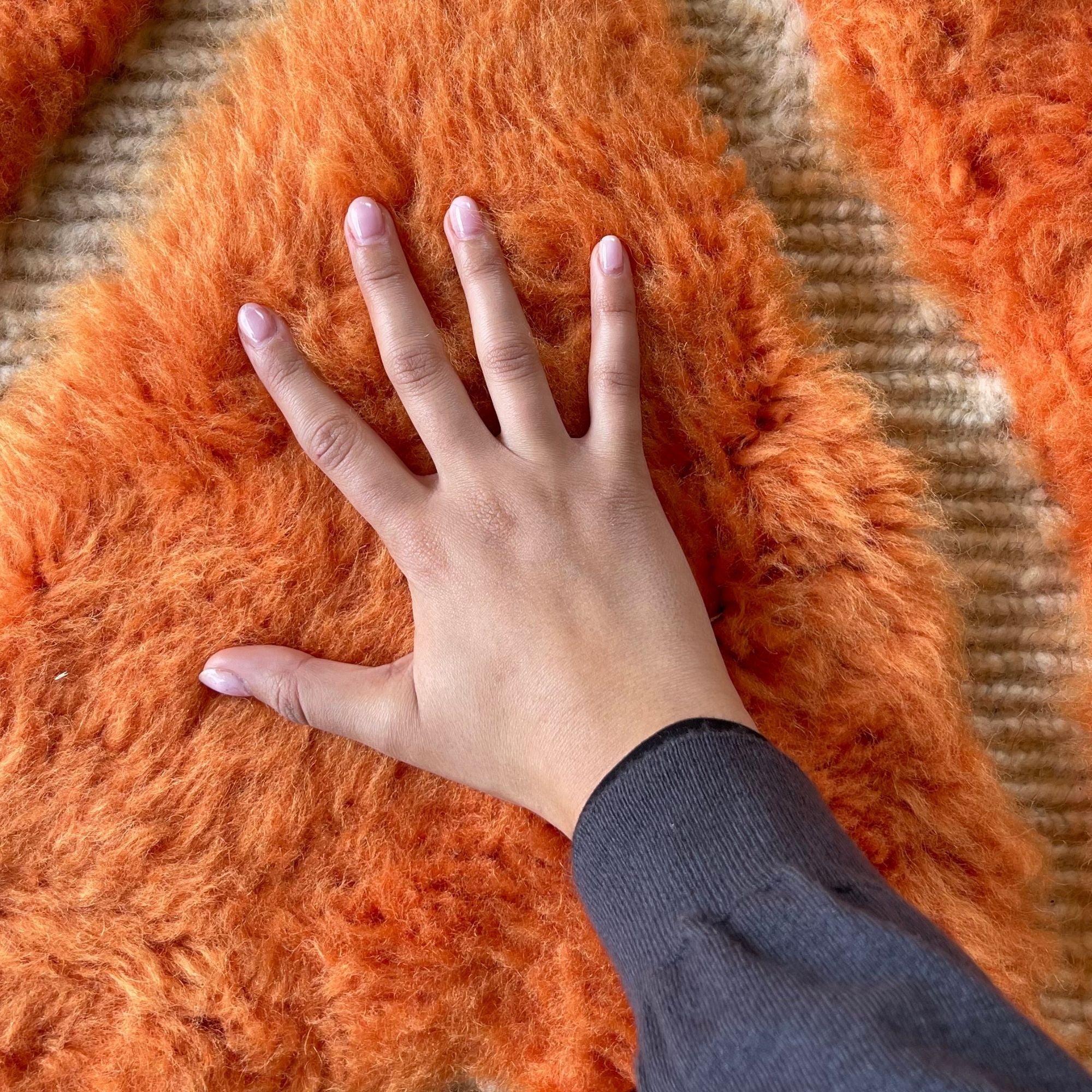 Hand touching the thick plush wool pile of Sahara Symphony No. 01 to demonstrate its luxurious softness.