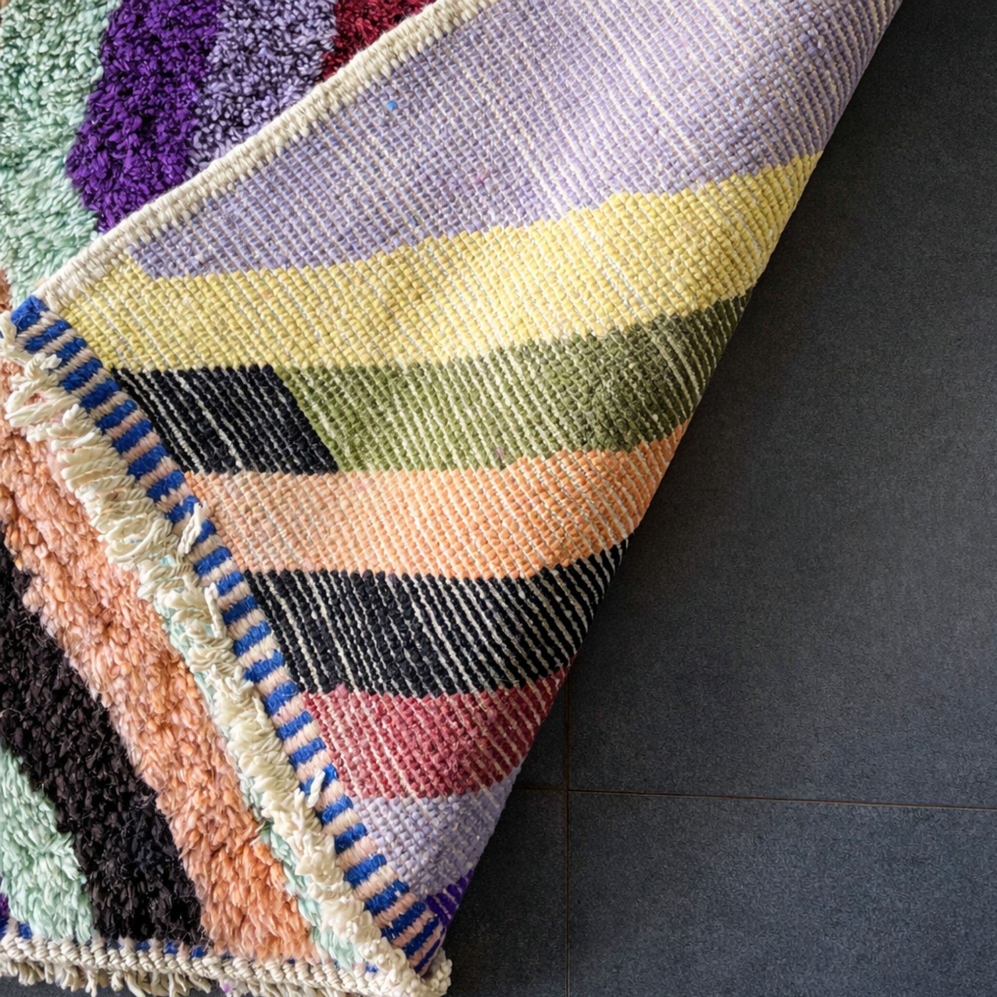 Handwoven Moroccan wool rug, Chorus design, folded corner showing flatwoven stripe pattern underside.