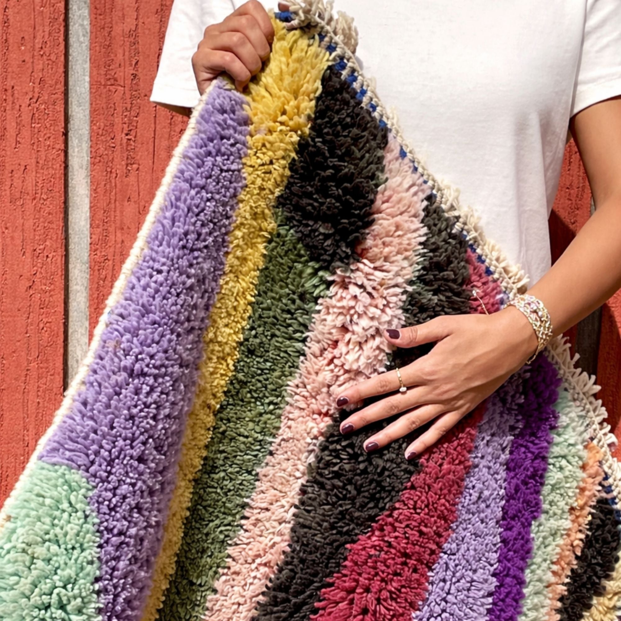Handwoven Moroccan wool rug, Chorus design, multicolor striped pile draped and held to show texture.