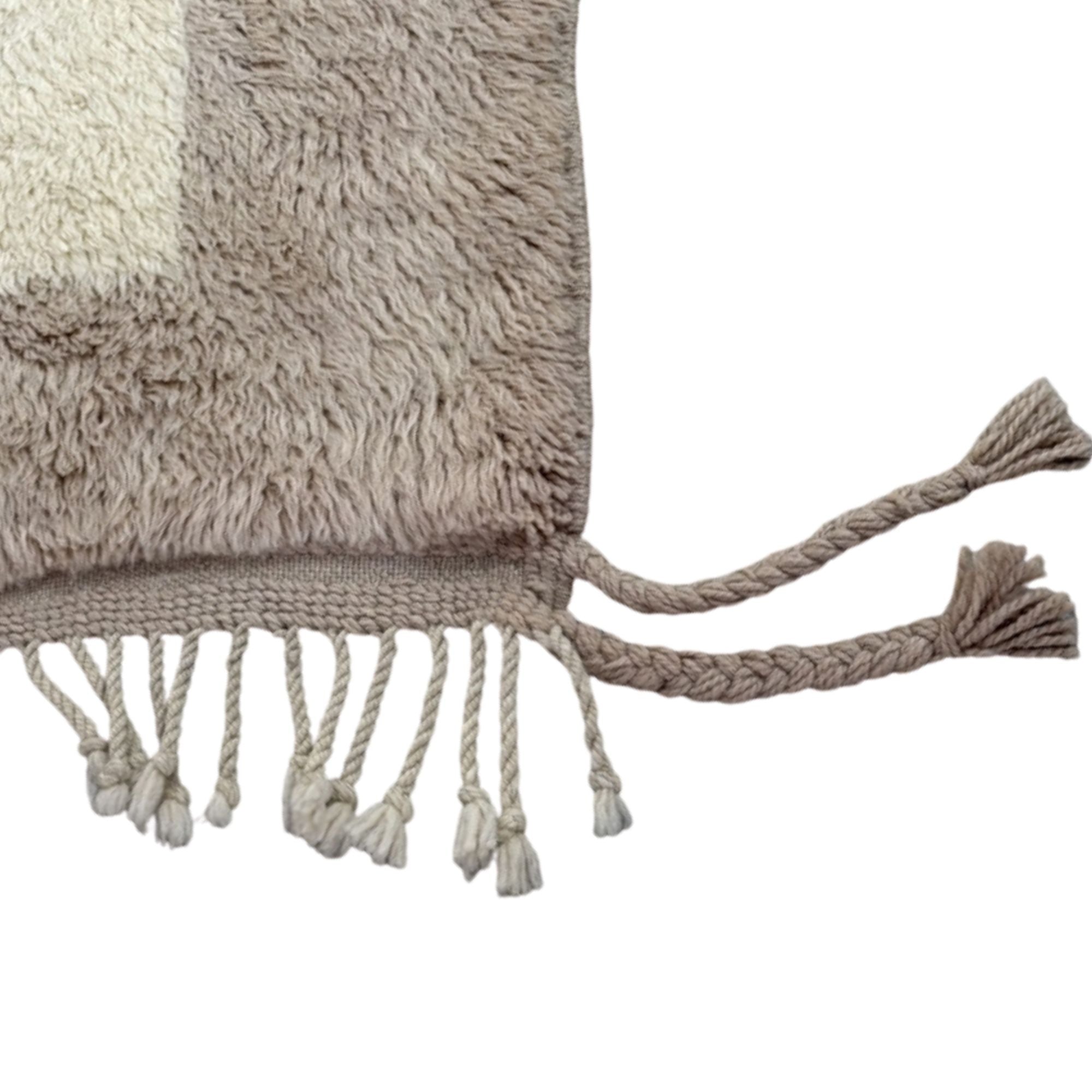Handwoven Moroccan wool rug, Meridian design, corner detail showing taupe border and braided tassel fringe.