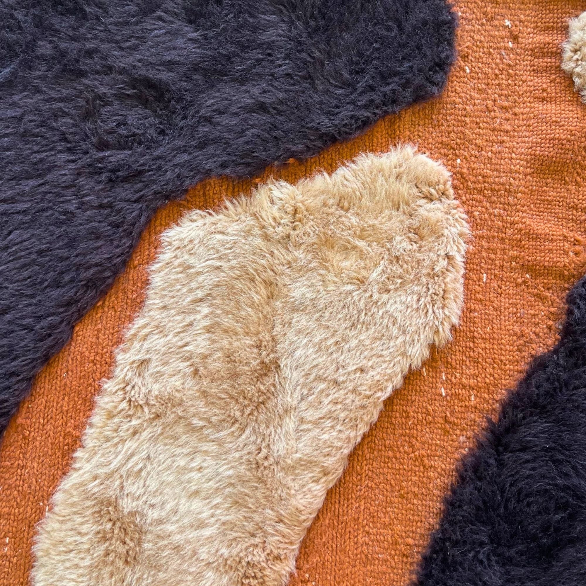 Handwoven Moroccan wool rug, Totem no. 01 design, close-up of cream and black wool shapes against rust ground.