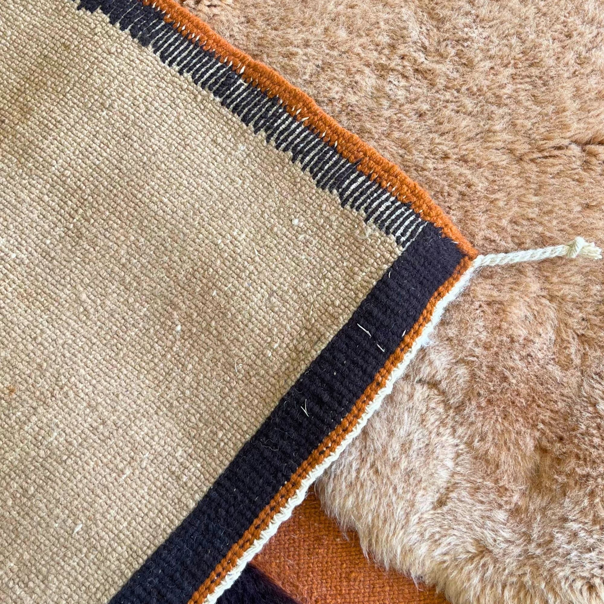 Handwoven Moroccan wool rug, Totem no. 01 design, corner detail with rust-orange border and fringe.