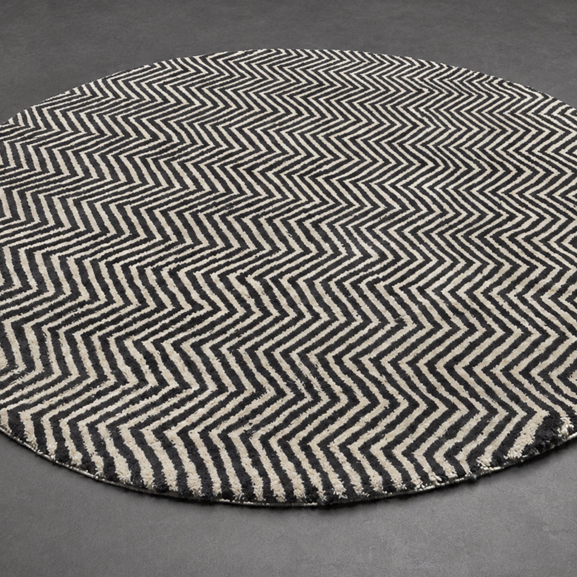 Handwoven Moroccan wool rug, Undertow design, black and ivory chevron pattern shown at an angle on dark flooring.