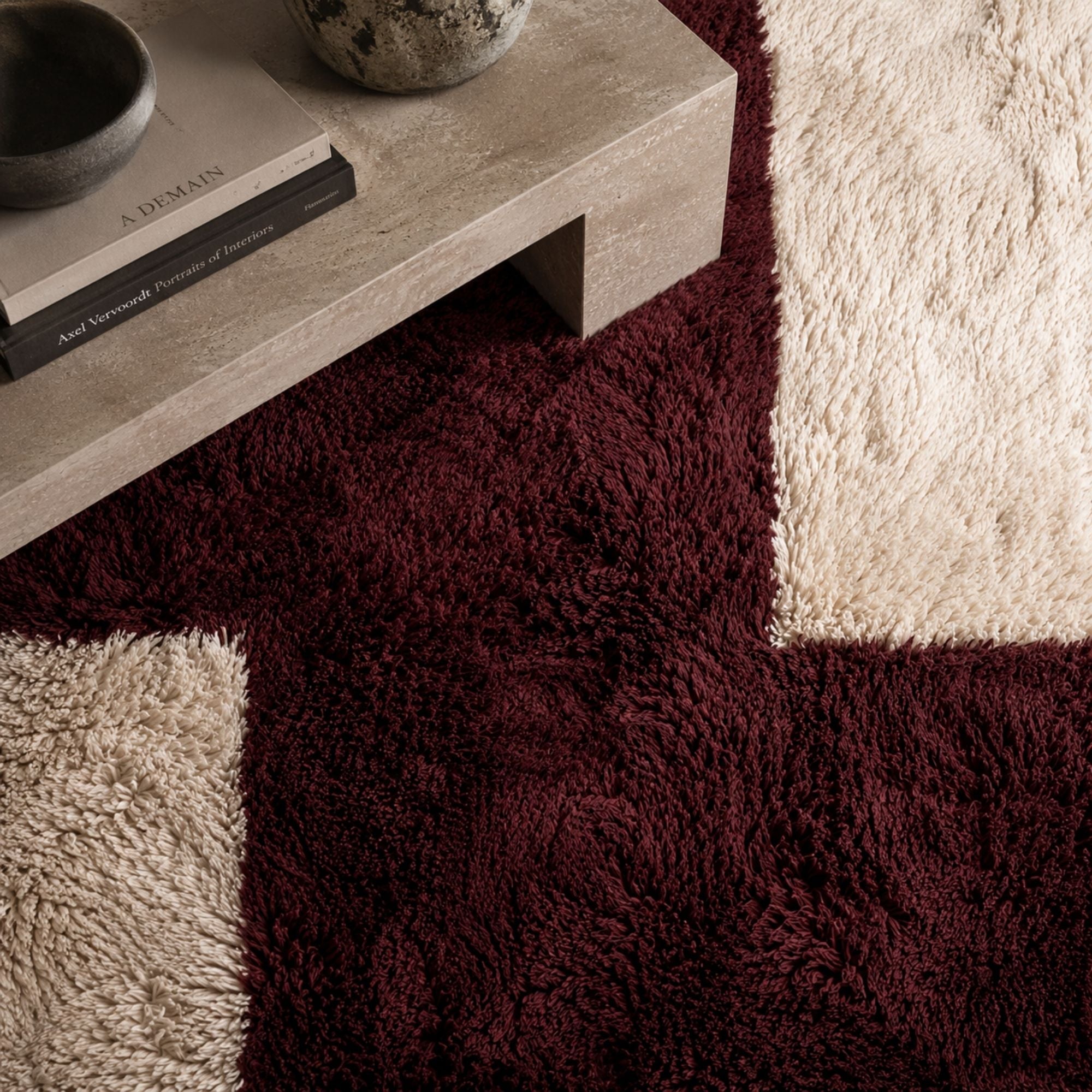 Modern stone coffee table styled over a burgundy and ivory geometric Moroccan rug with rich wool texture, deep color saturation, and contemporary luxury aesthetic.