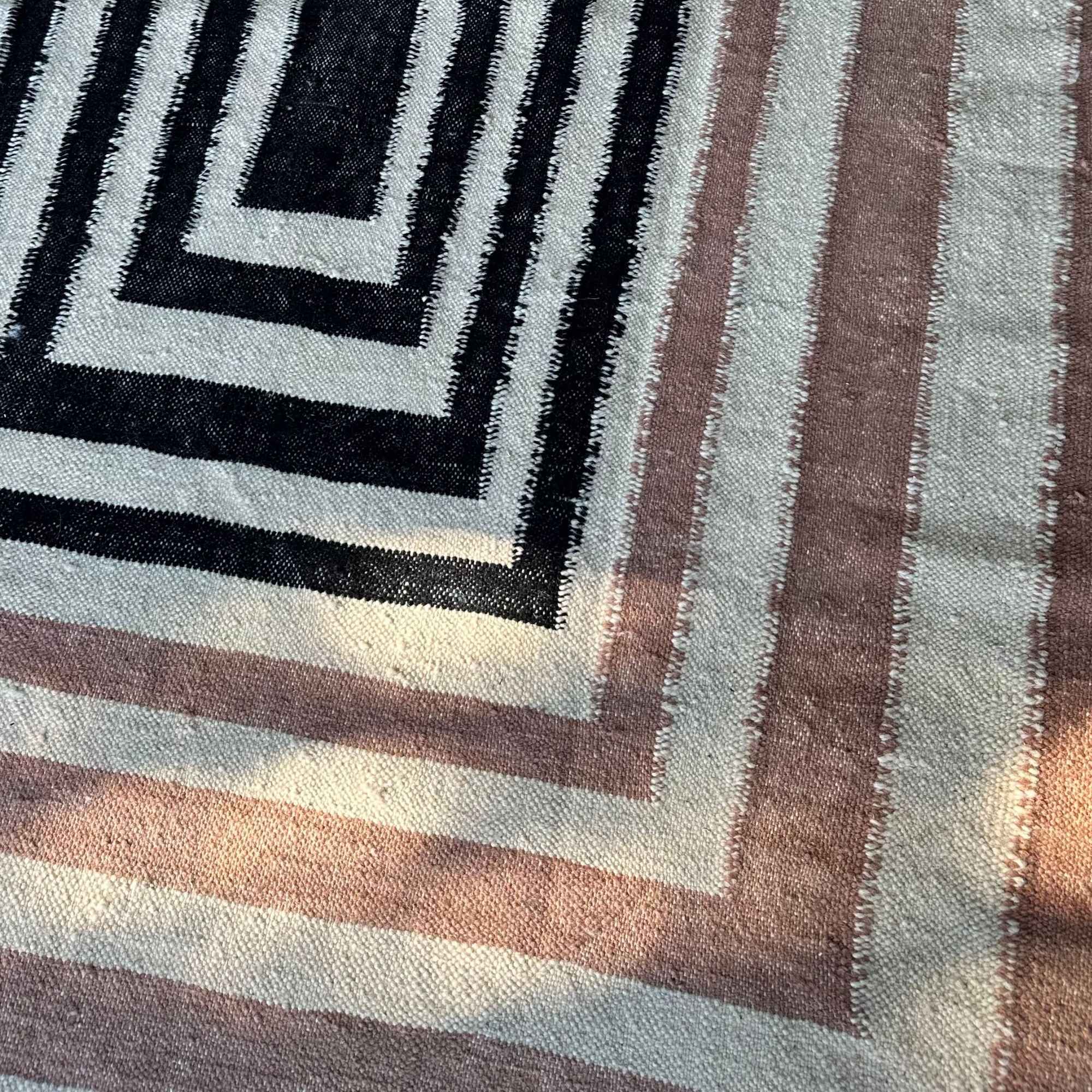 Mystique Beauty flat weave rug with black and brown geometrical patterns on an off-white base.