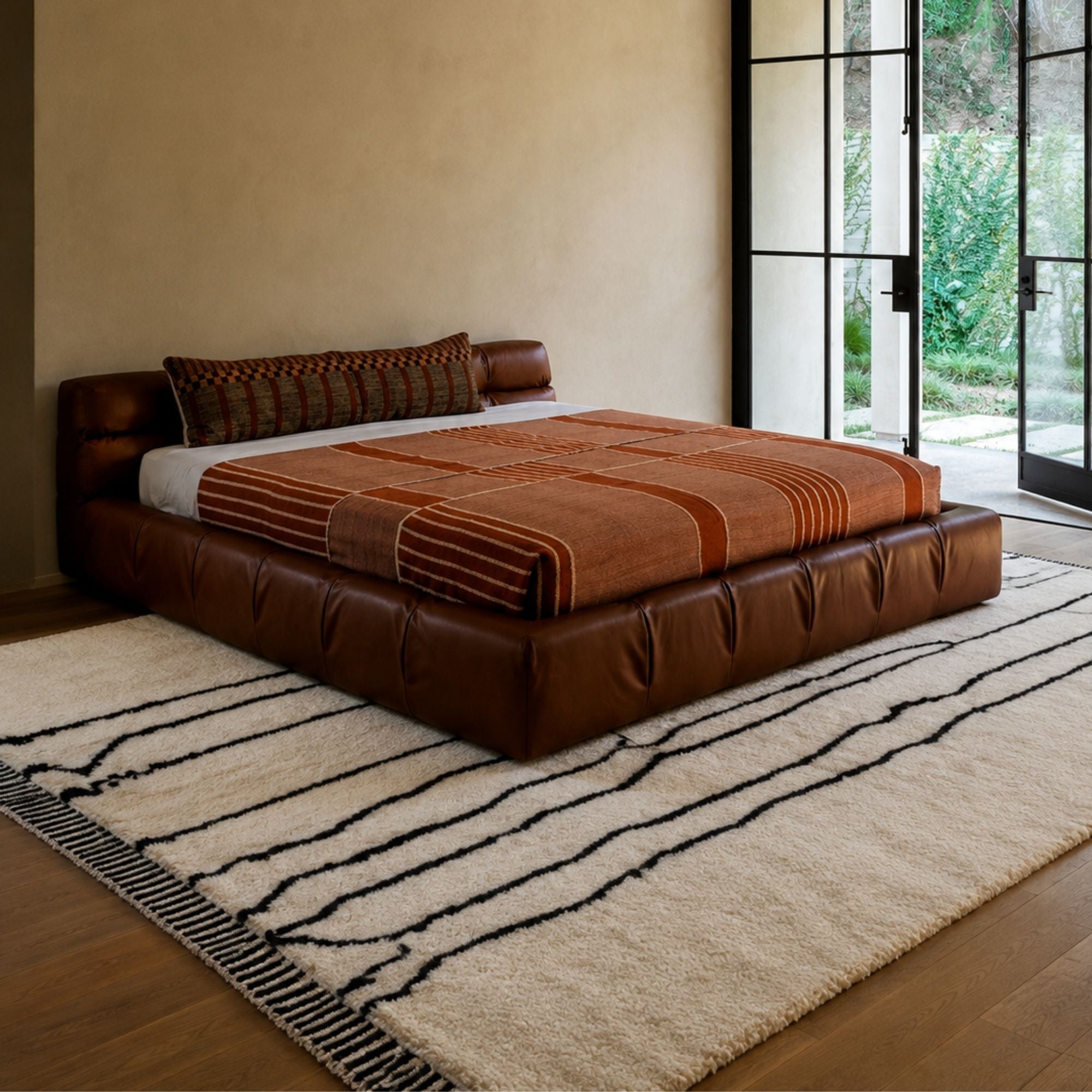 Reed Line handmade Moroccan wool rug styled beneath a leather bed with a striped throw blanket.