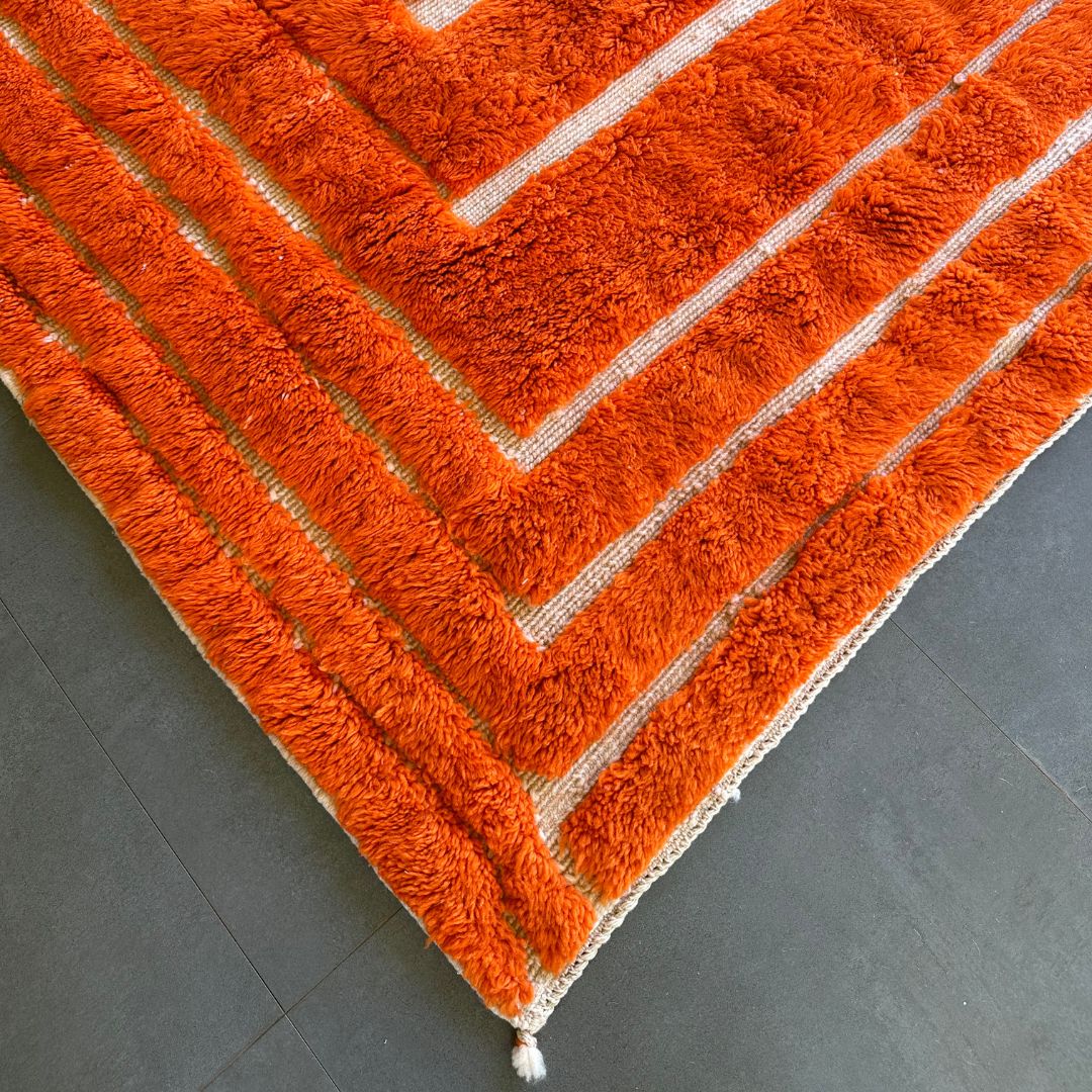 Sahara Symphony Moroccan rug in vibrant orange with a textured design revealing a white base