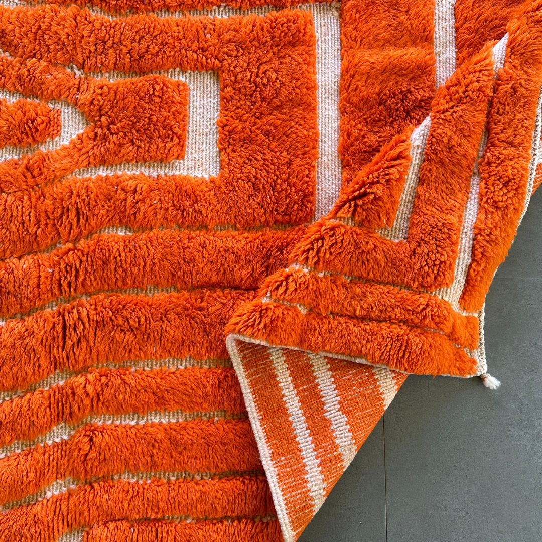 Sahara Symphony Moroccan rug in vibrant orange with a textured design revealing a white base