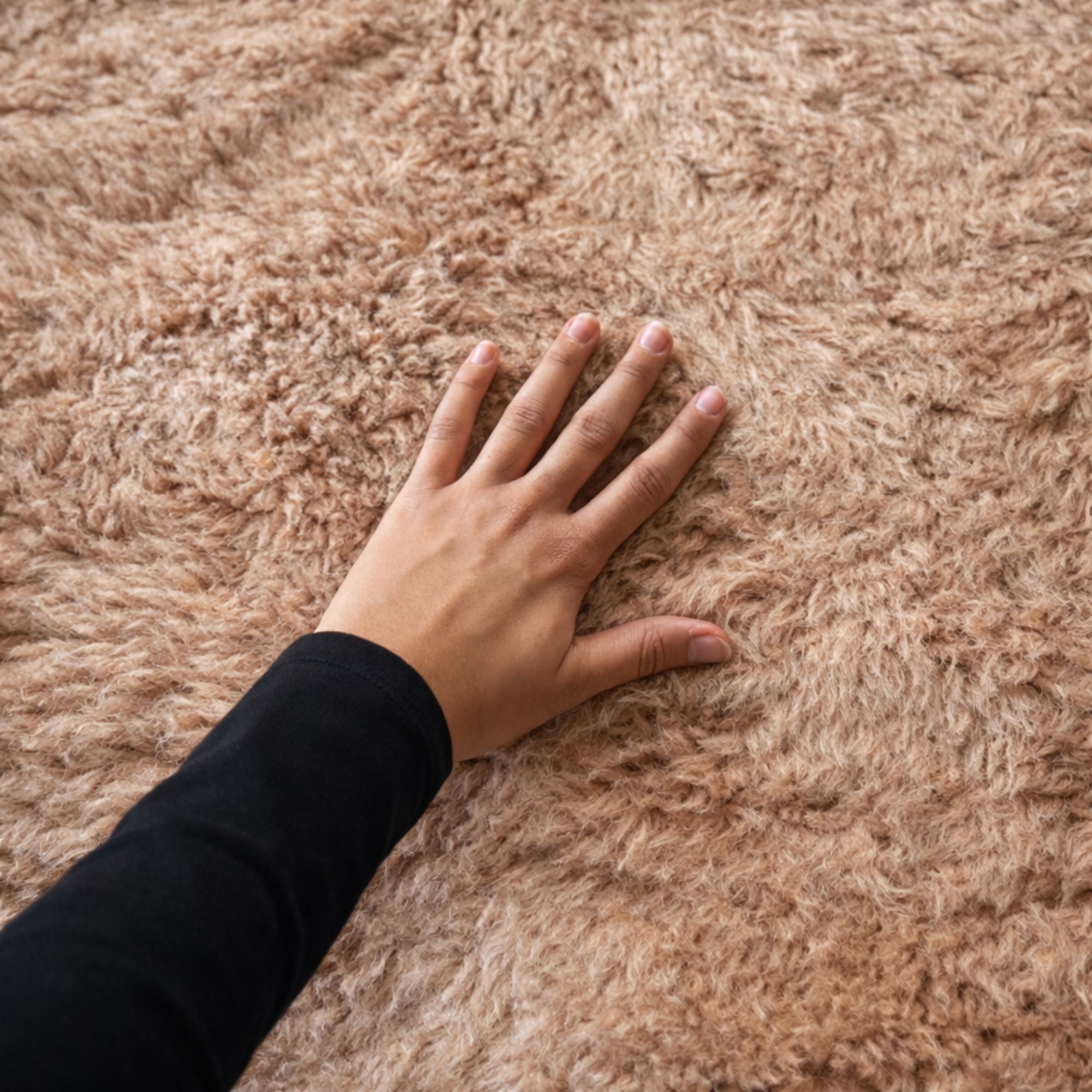Soft high pile detail of the Cadence rug with hand touching the ultra-plush natural wool texture in warm ivory tones.
