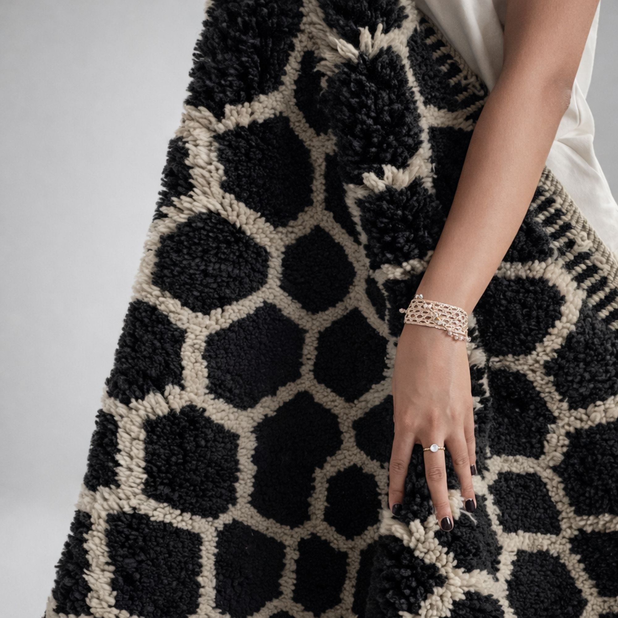 Woman holding a handmade Moroccan Beni Mrirt rug with black organic motifs on an ivory background. The image highlights the rug’s scale, softness, and luxurious wool texture.