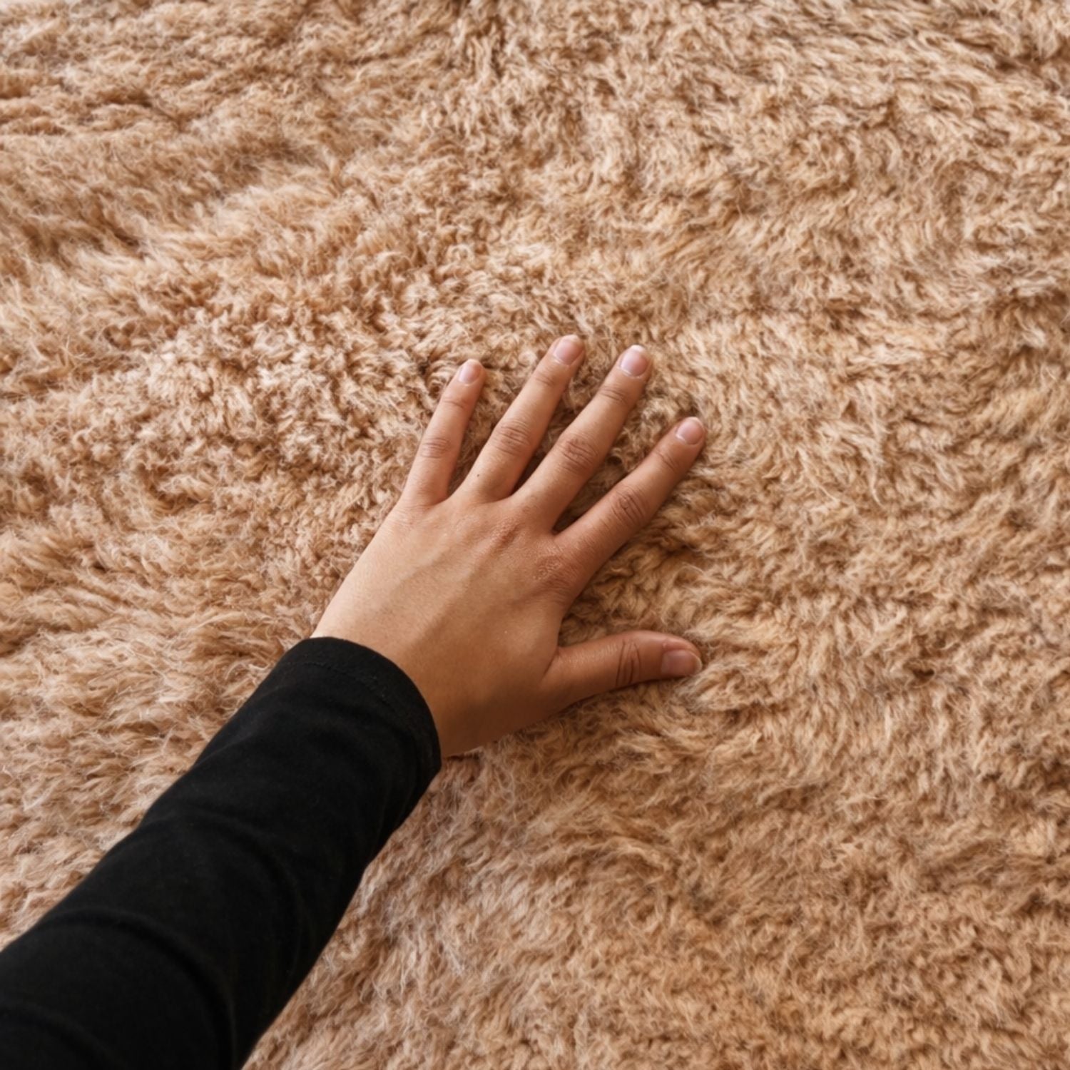 Close-up of a hand pressing into a soft high pile Moroccan Beni Mrirt rug in natural beige wool, showcasing texture and artisanal craftsmanship from the Atlas Mountains